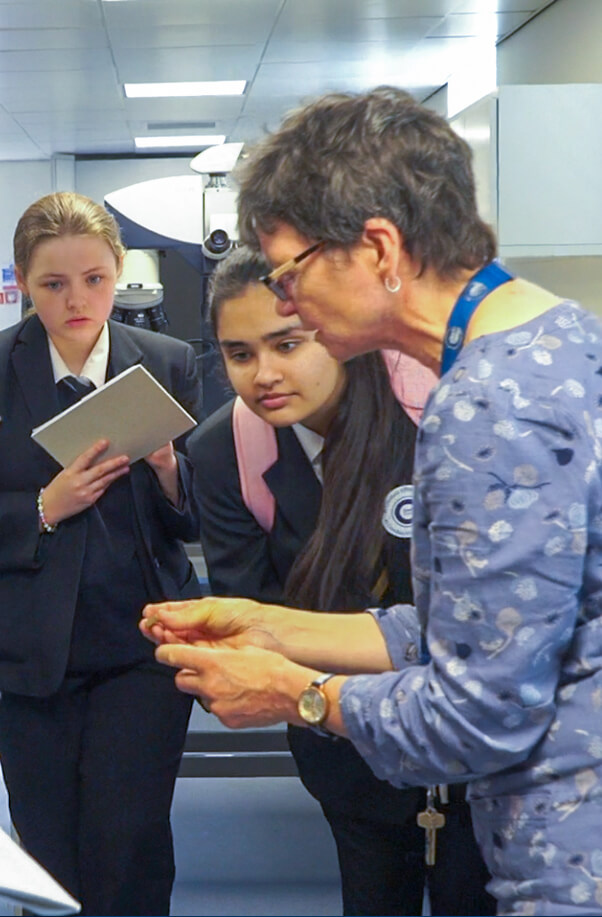 Picture of person showing something small to 2 secondary school students