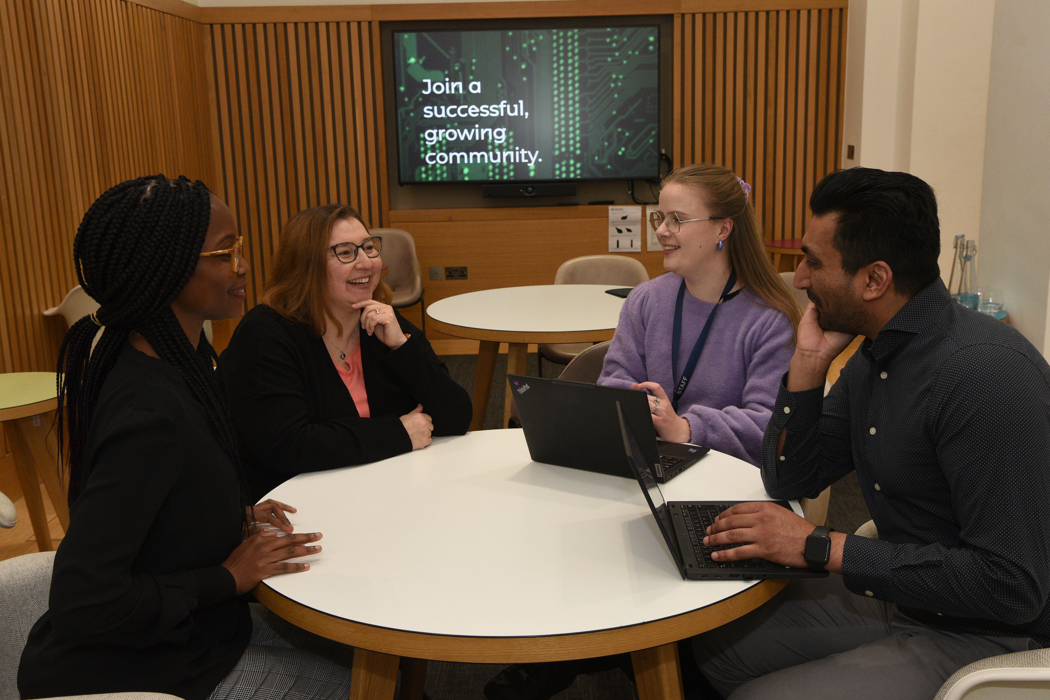 Three women and a man sitting around a table with laptops