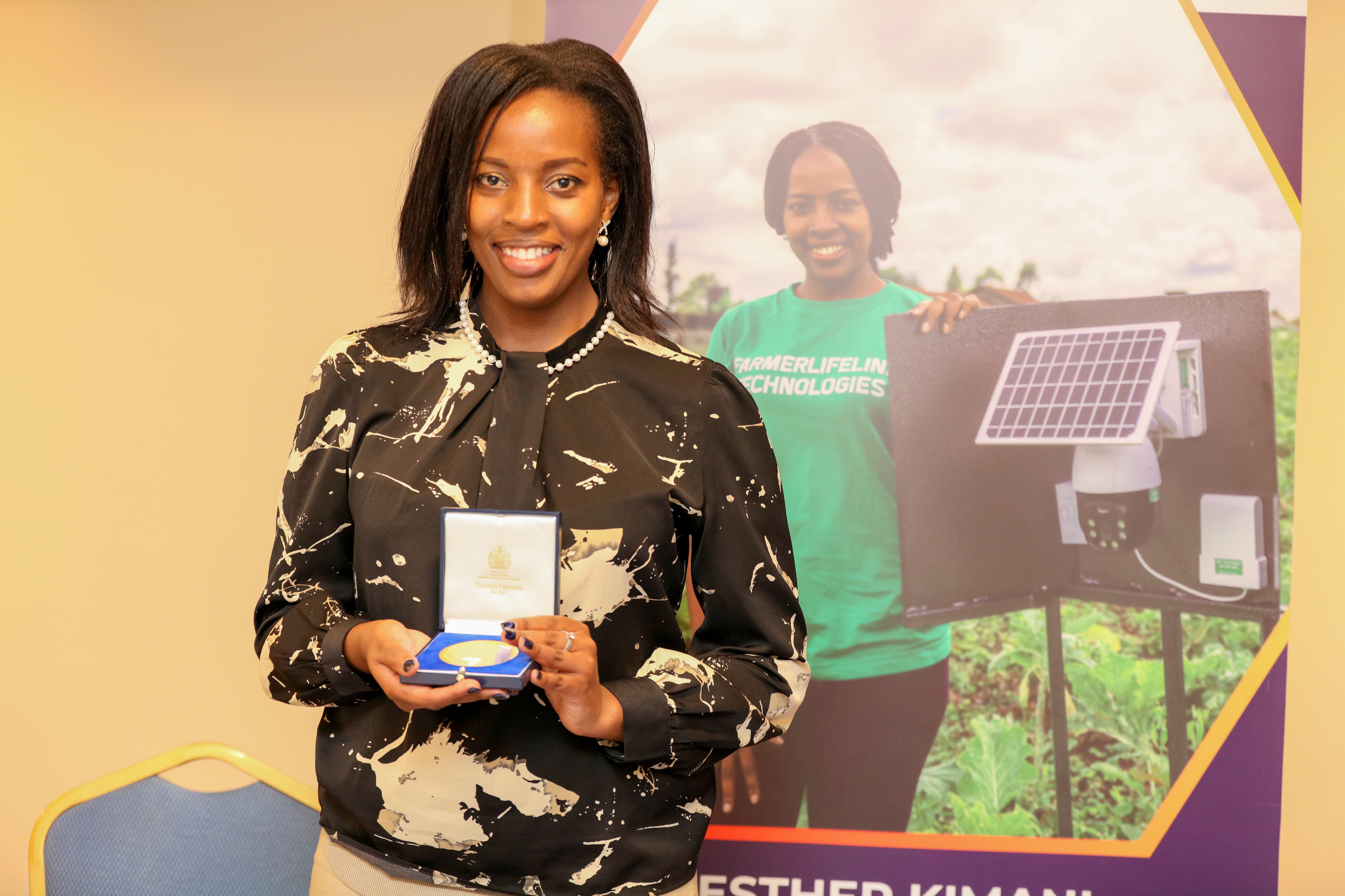 African woman entrepreneur holding trophy in front of photo of her engineering innovation