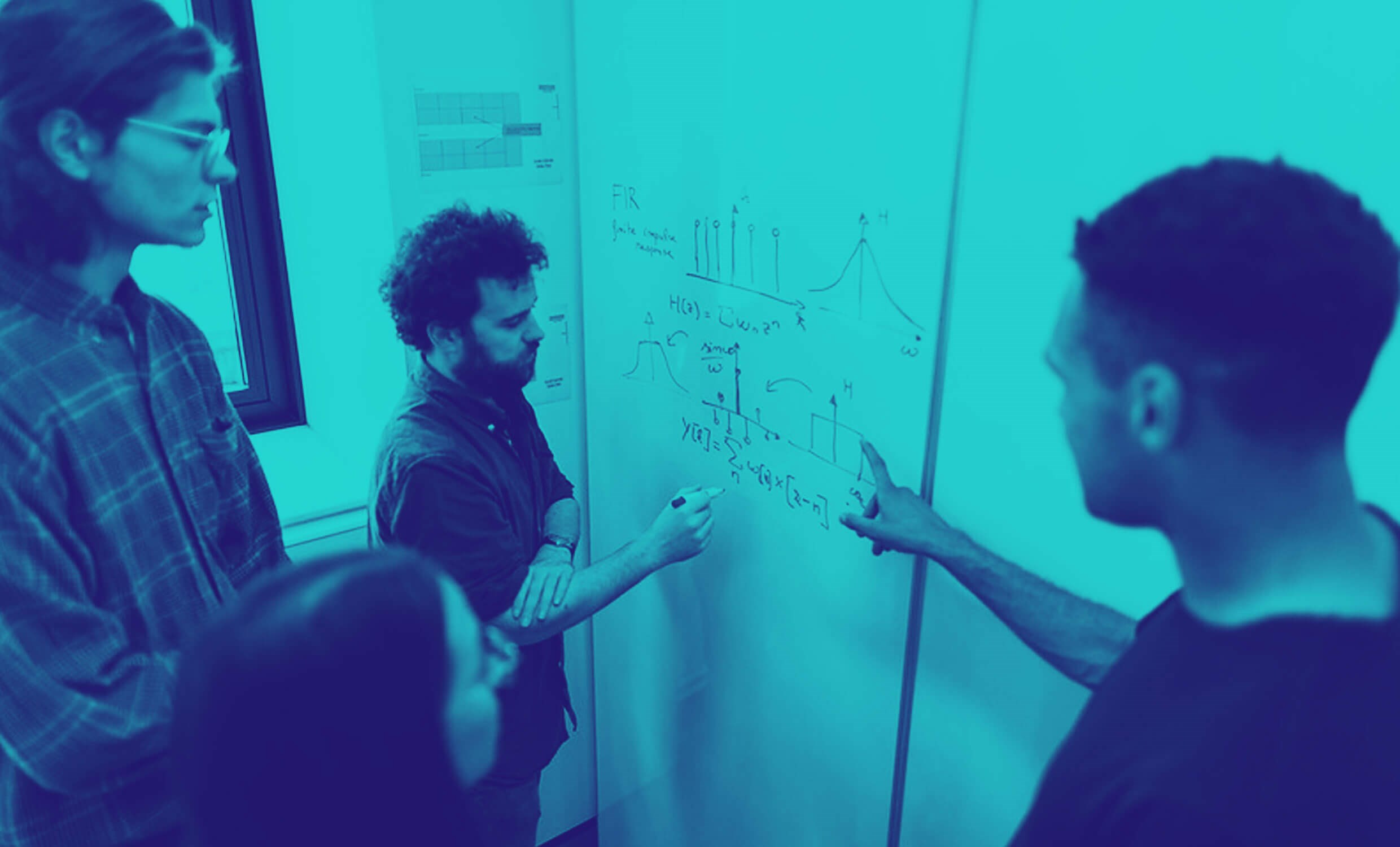 Four engineers are standing in front of a whiteboard, engaged in technical discussions over technical sketches.