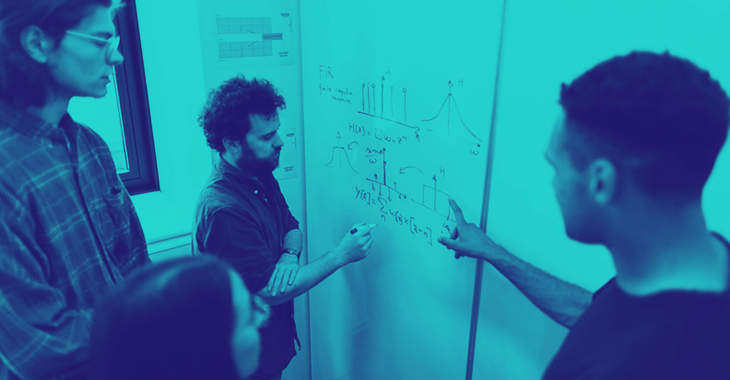 Group of engineers discussing technical sketches on a whiteboard.