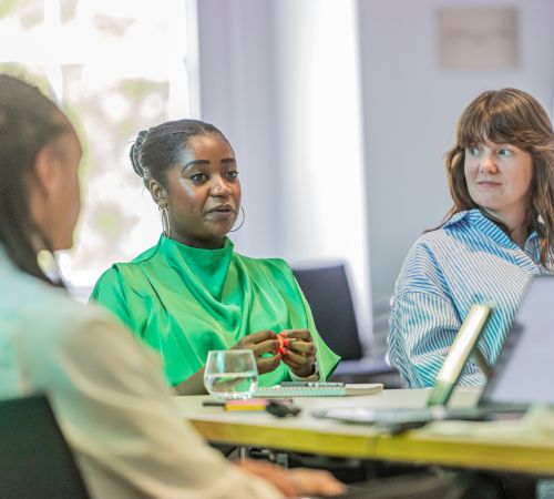 three women sit at a desk with laptops.